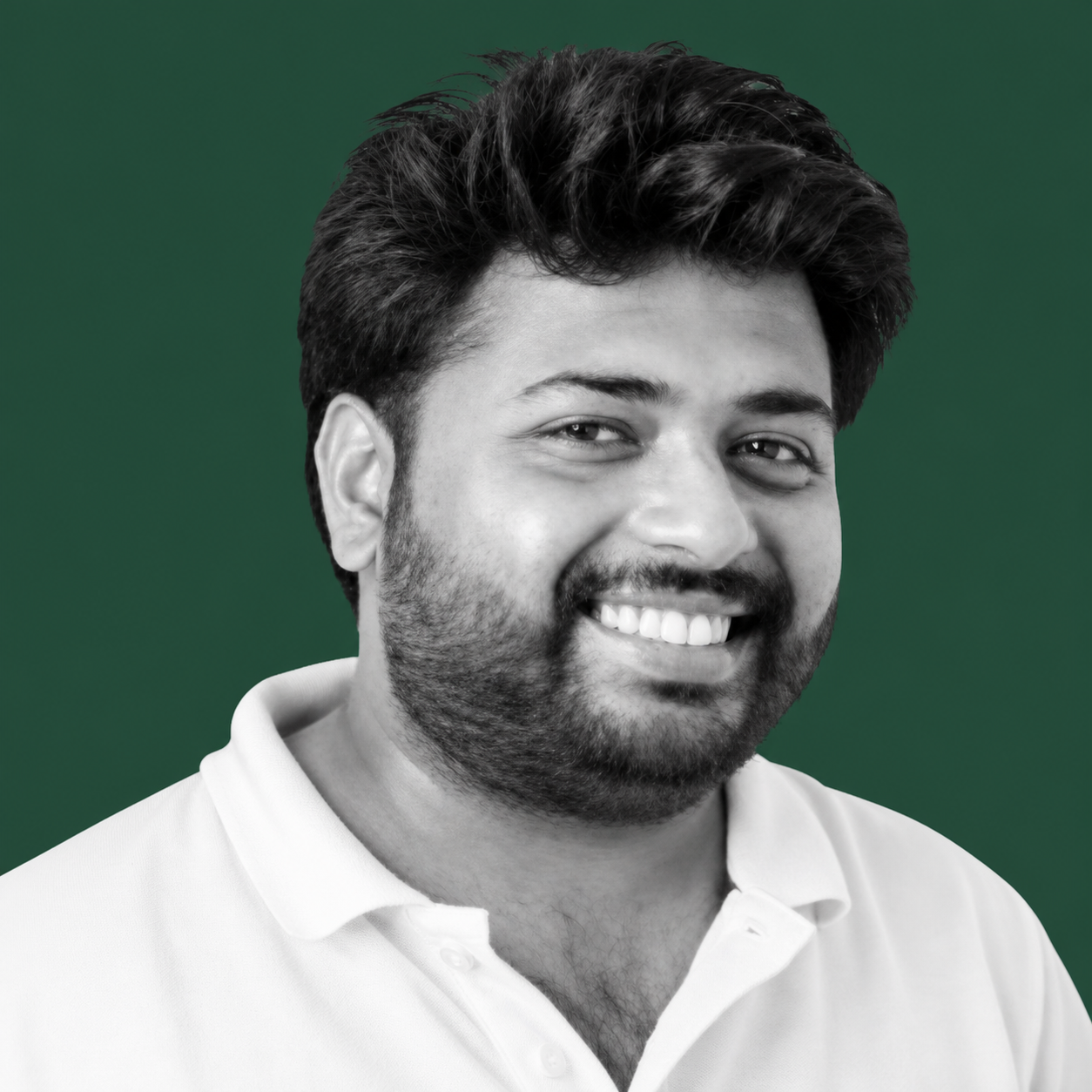 Monochrome editorial portrait of Dhawal Kulkarni smiling against a deep forest background